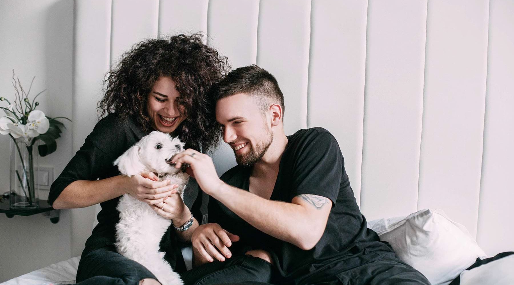 a man and woman sitting on a bed playing with a dog